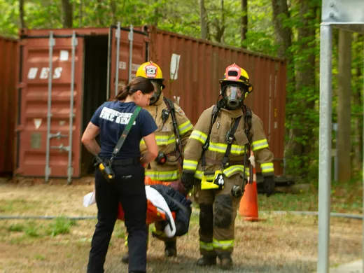 Pompiers en appareil respiratoire évacuant une victime sur un brancard, sous le regard d'un membre du service d'incendie