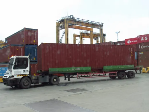 Tracteur portuaire tirant un conteneur devant les portiques d'un terminal à conteneurs