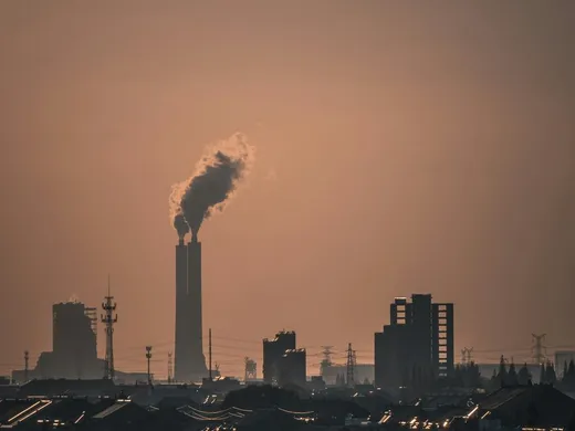Cheminée industrielle rejetant un panache de fumée sombre au-dessus d'une ville au crépuscule